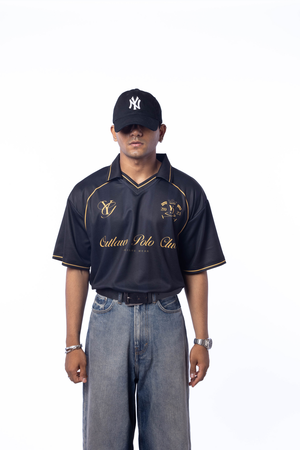 Man wearing a black and gold polo shirt with 'Yale Polo Club' branding, paired with a black cap and jeans on a white background.