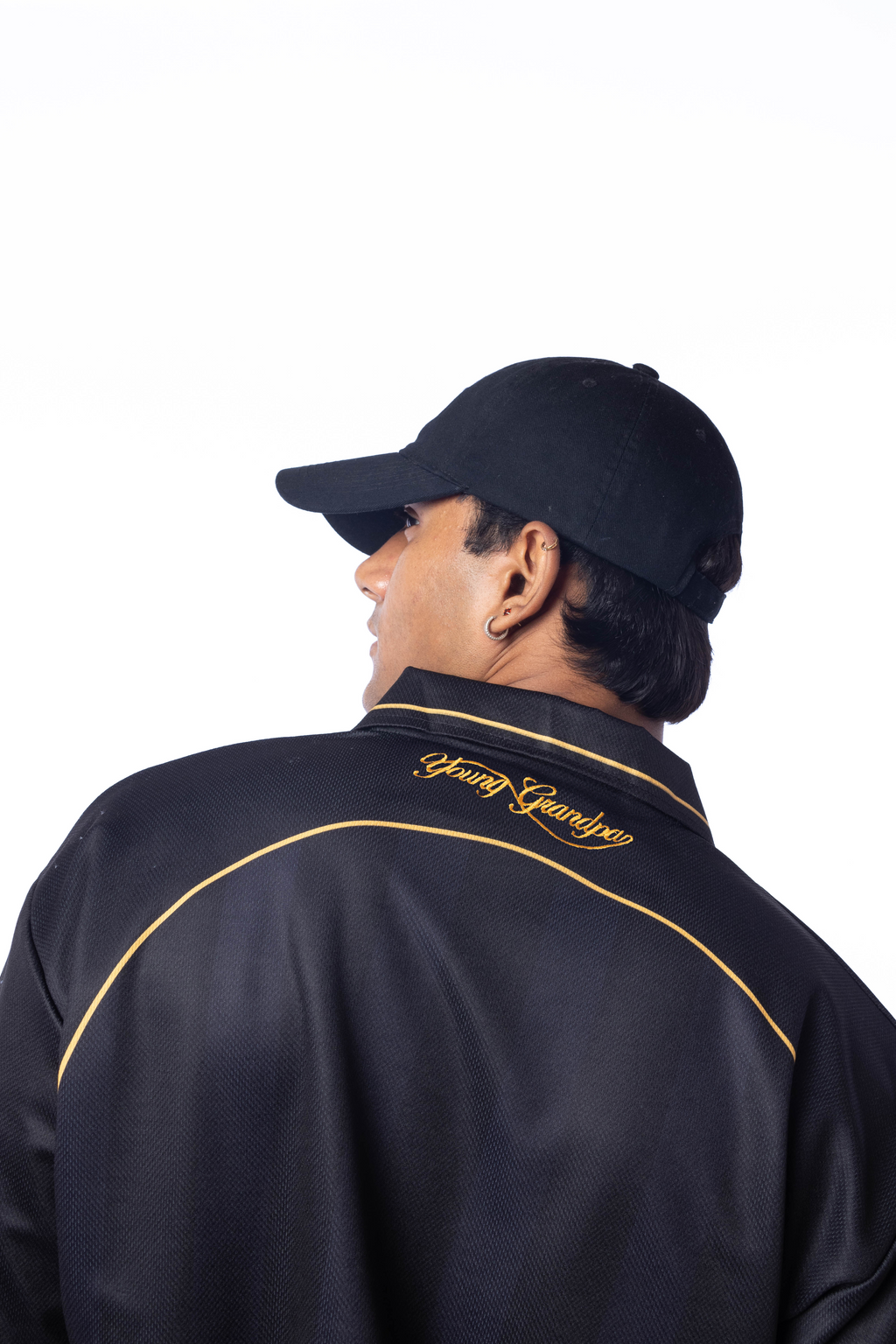 Person wearing a black jacket with gold accents and a cap on a white background