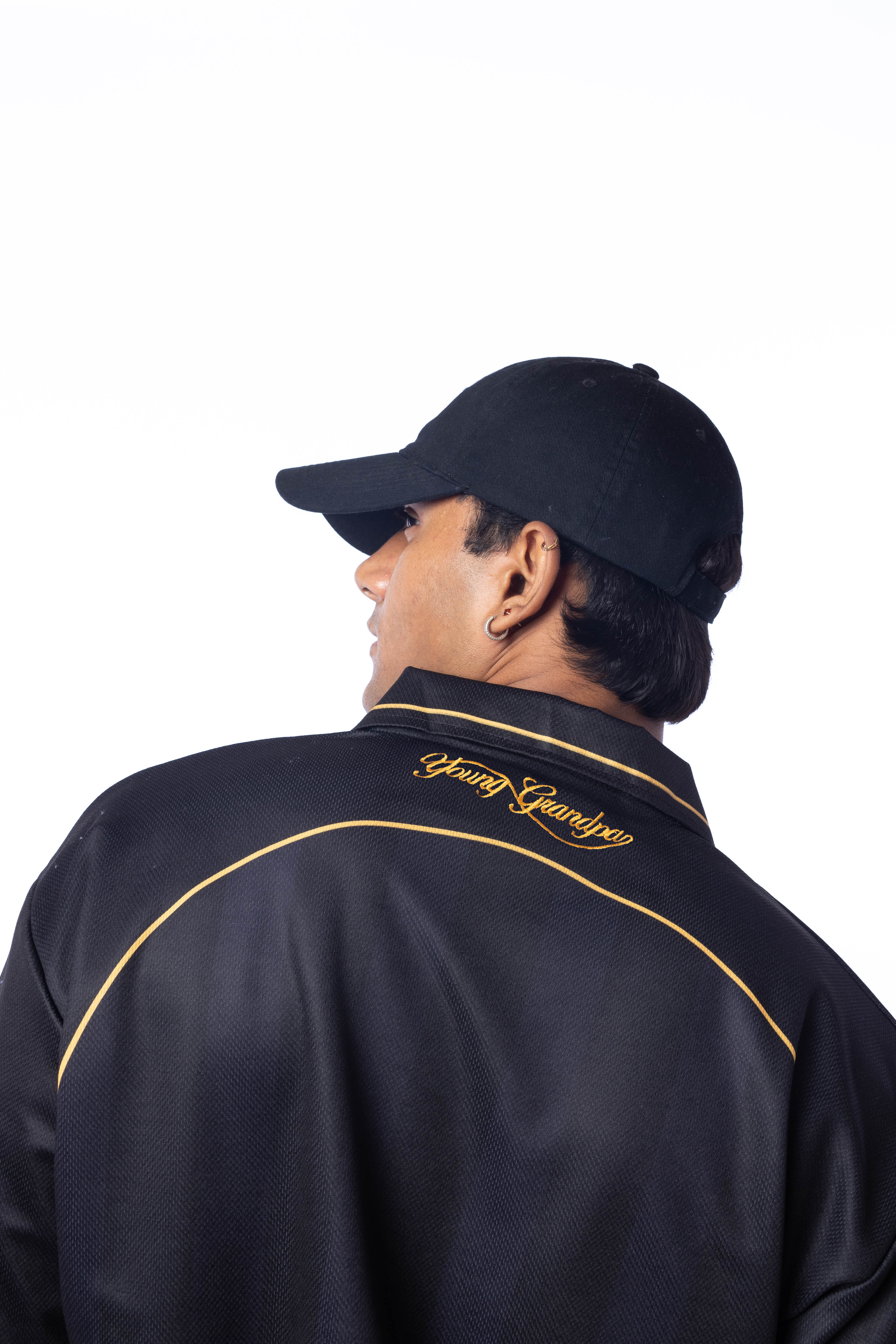 Person wearing a black jacket with gold accents and a cap on a white background